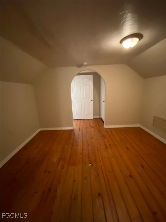 Bonus room with vaulted ceiling, hardwood / wood-style floors, and arched walkways