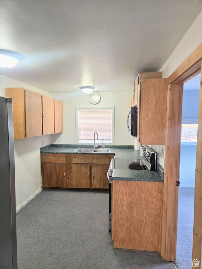 Kitchen featuring dark countertops, brown cabinets, appliances with stainless steel finishes, and dark colored carpet