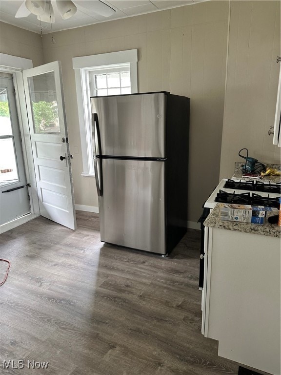 Kitchen with light stone counters, white cabinetry, dark hardwood / wood-style flooring, ceiling fan, and stainless steel fridge