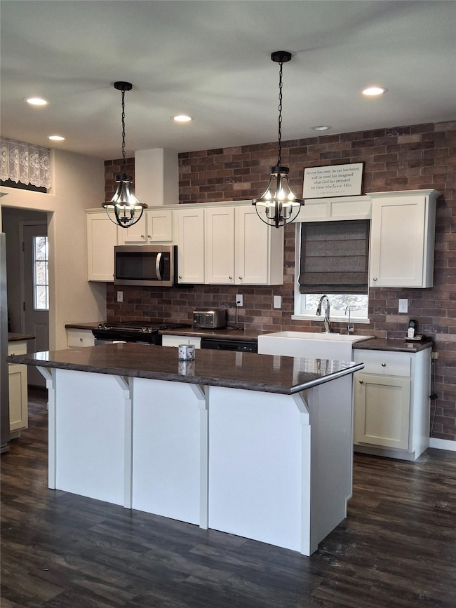 Kitchen featuring a chandelier, pendant lighting, dark wood-type flooring, stainless steel appliances, and dark stone counters