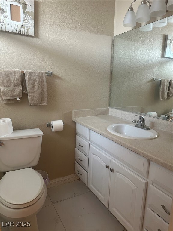 Bathroom with toilet, a textured wall, baseboards,