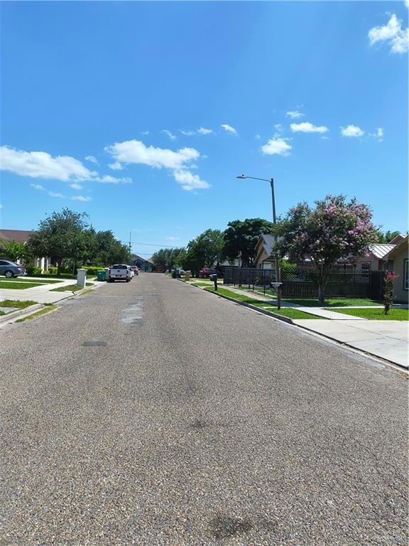 View of asphalt street featuring sidewalks, street lighting, and curbs