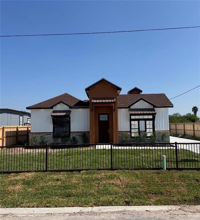 Modern inspired farmhouse with a fenced front yard, brick siding, roof with shingles, and board and batten siding