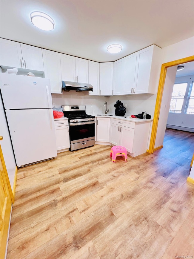 Kitchen with freestanding refrigerator, gas stove, white cabinets, light wood-type flooring, and light countertops