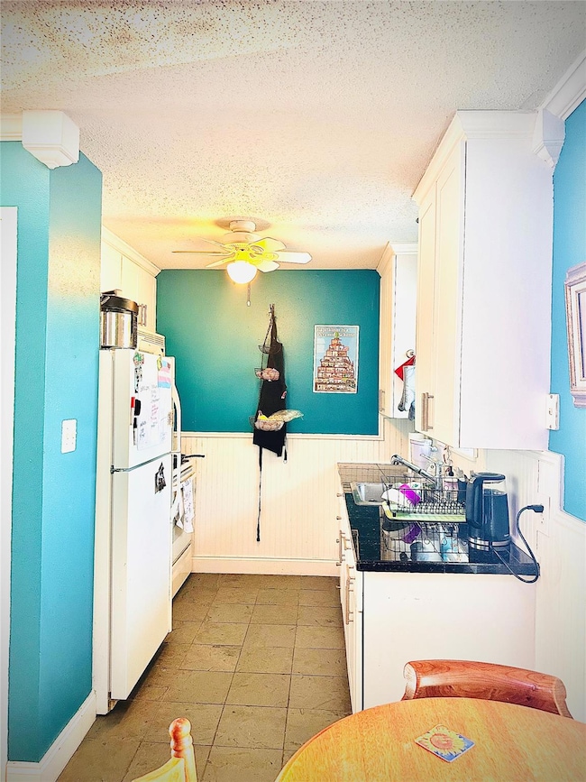 Kitchen with a wainscoted wall, white cabinetry, a textured ceiling, white appliances, and a ceiling fan