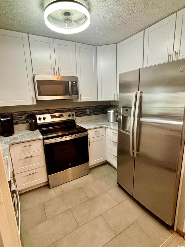 Kitchen featuring decorative backsplash, light tile patterned flooring, a textured ceiling, white cabinets, and appliances with stainless steel finishes