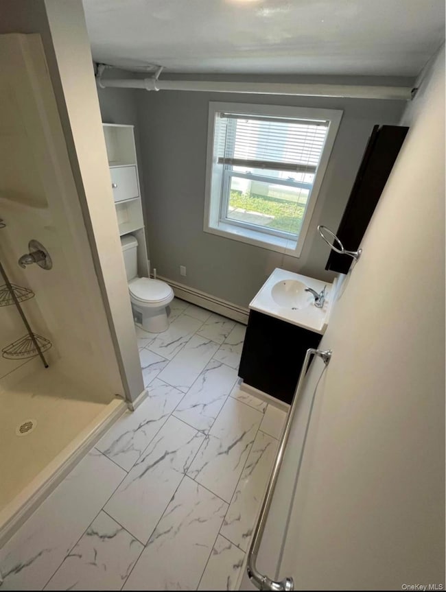 Bathroom featuring vanity, a shower stall, light marble finish floors, and a baseboard radiator