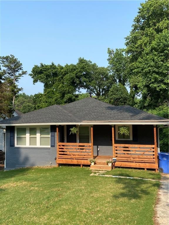 View of front of home with brick siding, covered porch, a front lawn, and roof with shingles