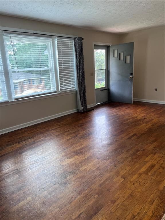 Empty room featuring dark wood-style flooring, a textured ceiling, and baseboards