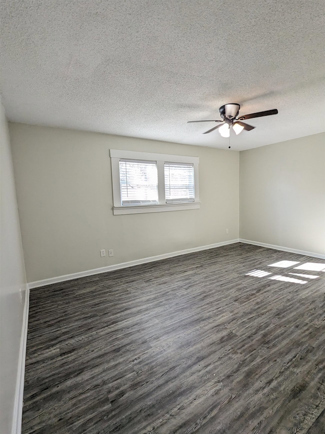 Spare room featuring dark wood-type flooring, ceiling fan, and a textured ceiling