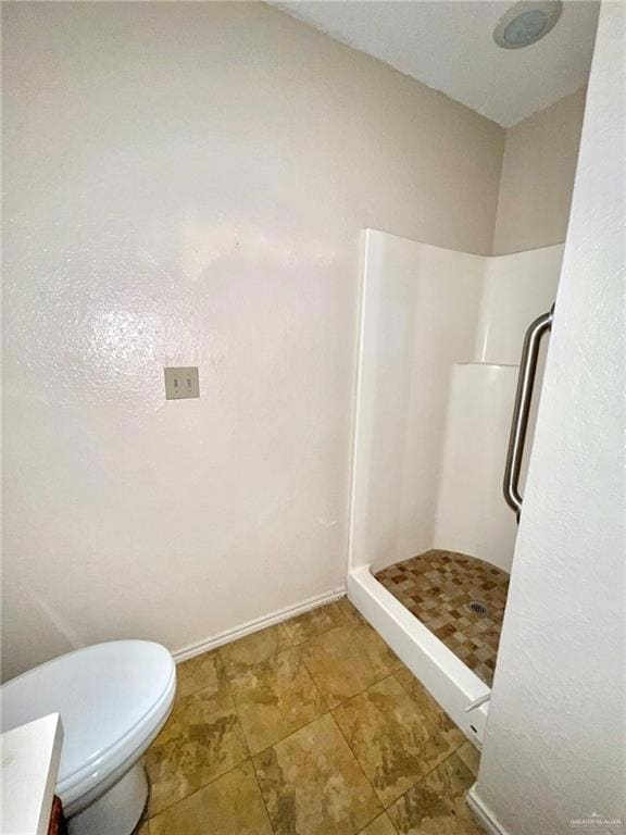 Bathroom featuring a shower stall, toilet, and baseboards