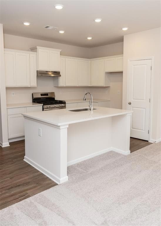 Kitchen featuring stainless steel gas range oven, under cabinet range hood, a sink, white cabinets, and an island with sink