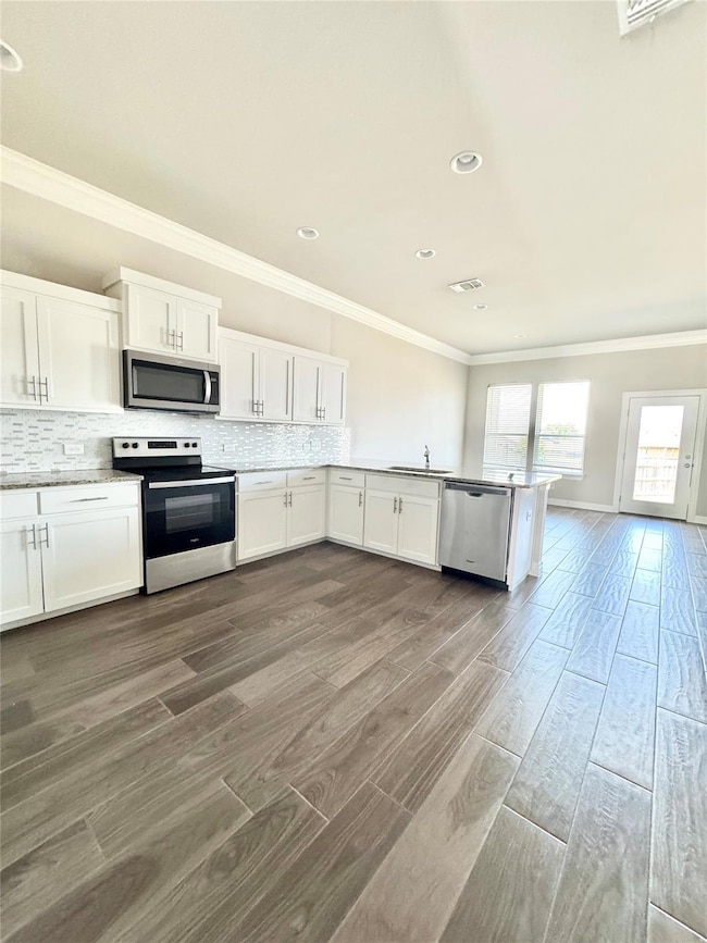 Kitchen featuring white cabinets, ornamental molding, stainless steel appliances, wood tiled floors, and tasteful backsplash