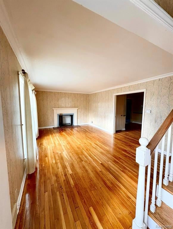 Unfurnished living room with light wood finished floors, wallpapered walls, crown molding, a fireplace, and stairs