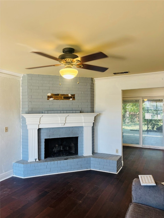 Unfurnished living room with crown molding, a brick fireplace, dark wood-style flooring, and a ceiling fan
