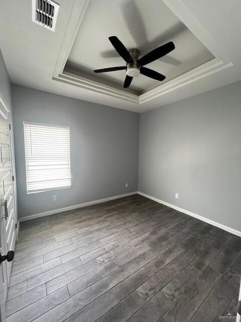 Empty room featuring dark hardwood / wood-style flooring, ceiling fan, and a tray ceiling