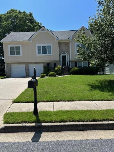 Raised ranch with a garage, driveway, a front yard, and stucco siding