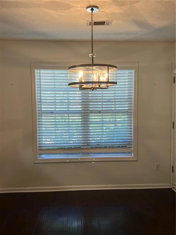 Unfurnished dining area with dark wood-style floors, a textured ceiling, and a chandelier