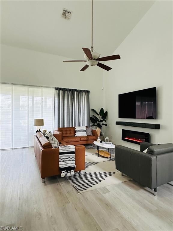 Living room featuring wood finished floors, a ceiling fan, high vaulted ceiling, and a lit fireplace