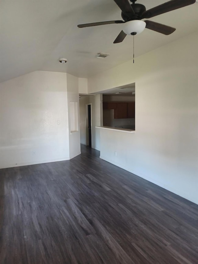 Spare room featuring dark wood finished floors, vaulted ceiling, and ceiling fan