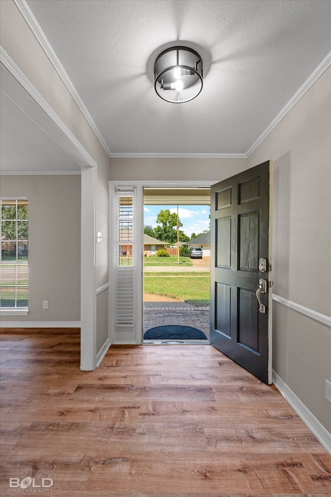 Foyer entrance with crown molding, light wood finished floors, and a textured ceiling