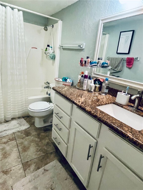 Bathroom featuring toilet, vanity, a textured wall