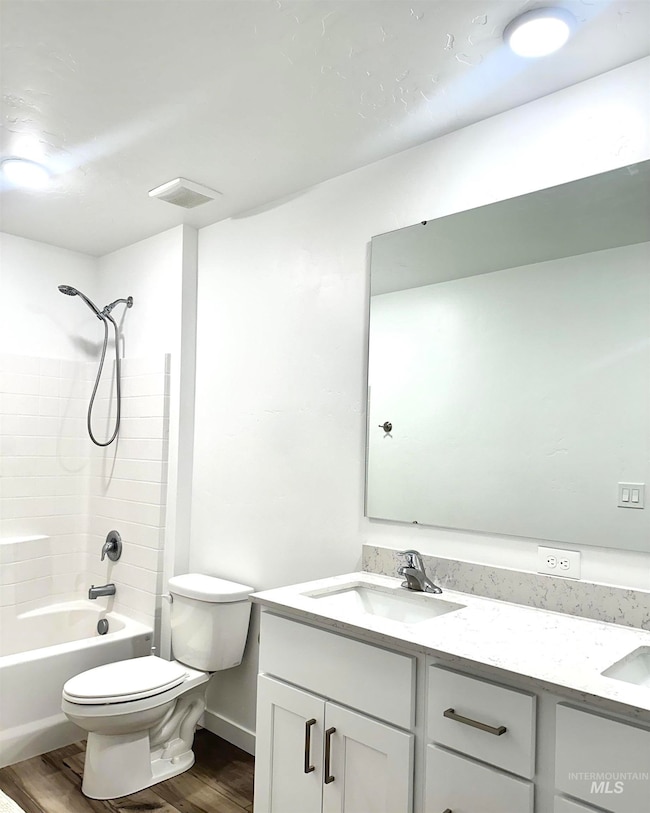 Bathroom with shower / bathtub combination, double vanity, and dark wood-type flooring