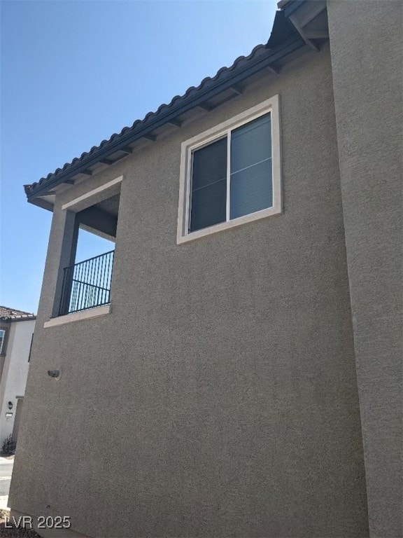 View of property exterior with stucco siding, a balcony, and a tiled roof