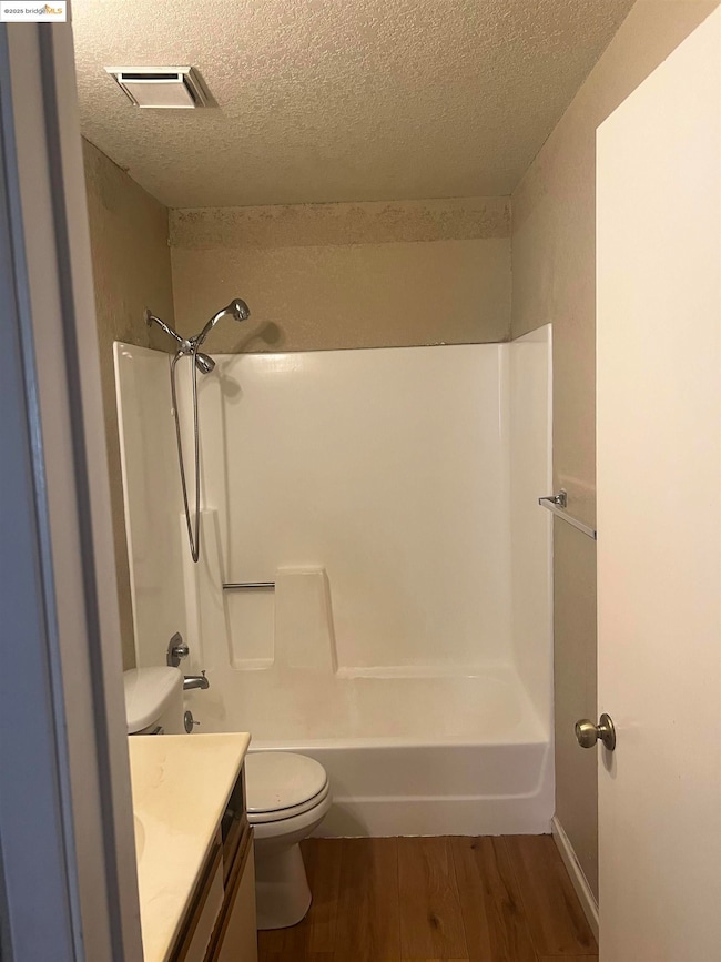 Full bath featuring vanity, a textured ceiling, wood finished floors, and shower / washtub combination