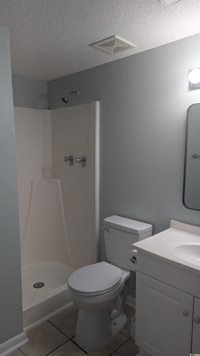 Bathroom with walk in shower, vanity, toilet, tile patterned flooring, and a textured ceiling