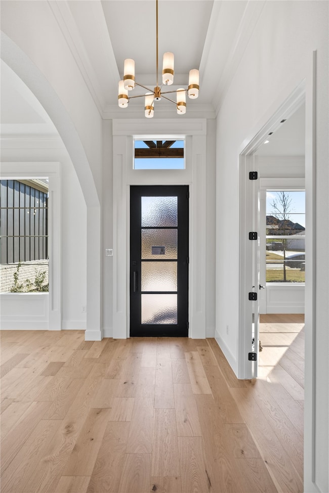 Foyer entrance with arched walkways, light wood-type flooring, and ornamental molding
