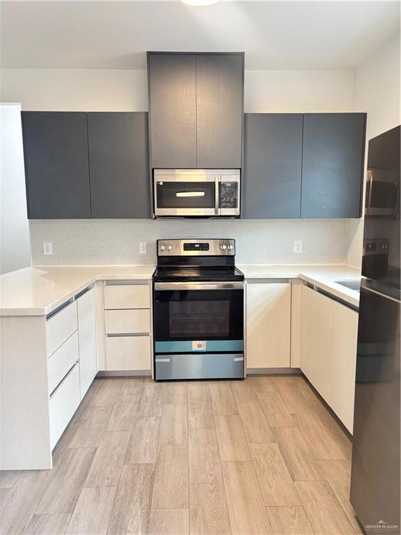 Kitchen featuring stainless steel range with electric stovetop, refrigertator, light wood-type flooring, light countertops, modern cabinets, and backsplash