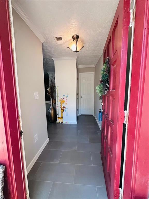 Foyer entrance featuring dark tile patterned floors, baseboards, a textured ceiling, and ornamental molding