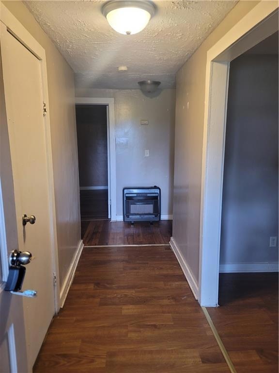 Hallway with wood finished floors, a textured ceiling, and heating unit