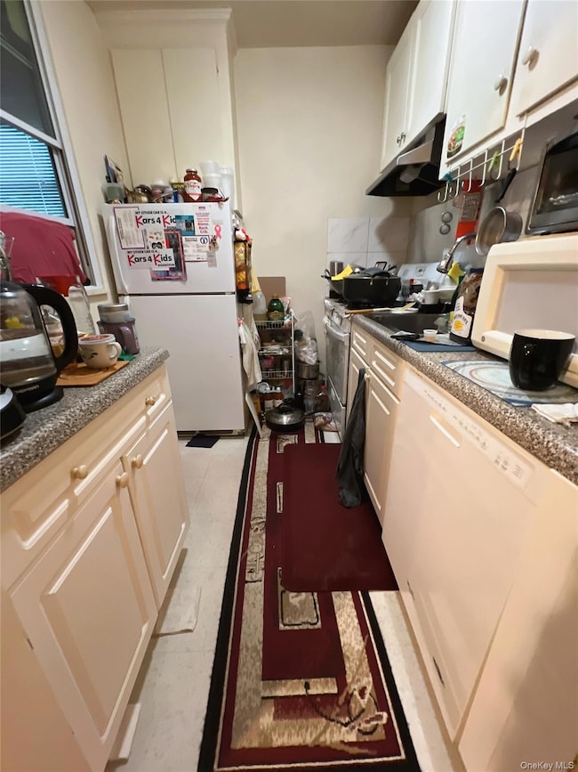 Kitchen featuring white appliances, white cabinets, backsplash, and under cabinet range hood