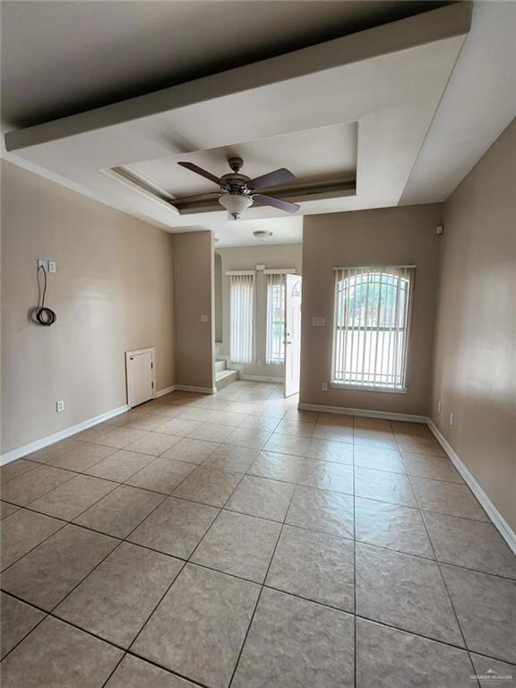 Tiled empty room featuring ceiling fan and a raised ceiling