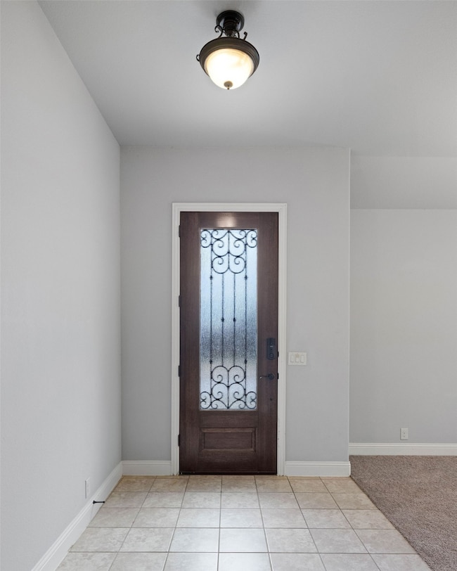 Foyer entrance featuring baseboards, light tile patterned floors, and light carpet
