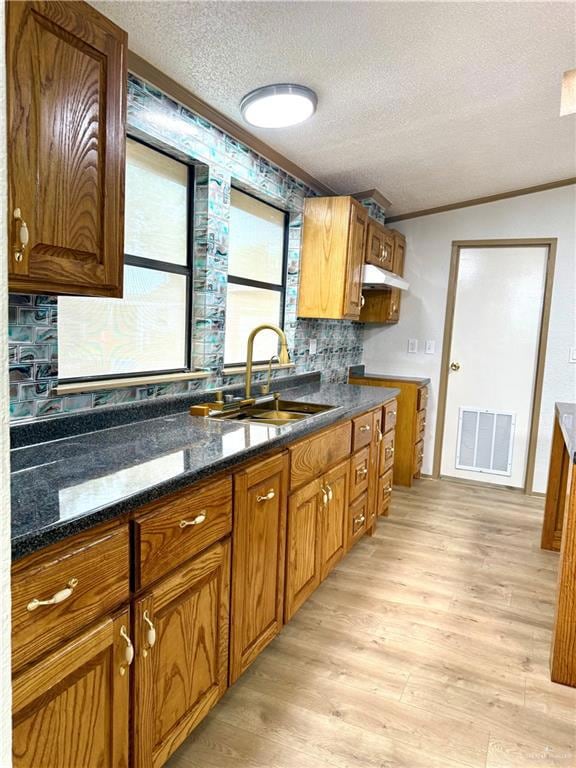 Kitchen featuring ornamental molding, a textured ceiling, light wood-type flooring, brown cabinetry, and under cabinet range hood