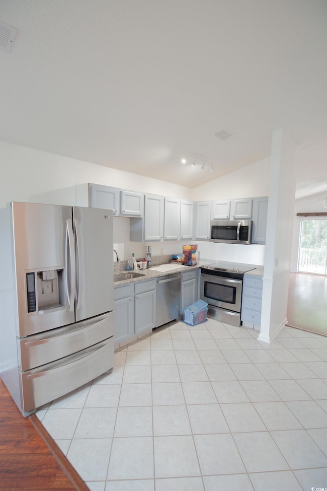 Kitchen featuring stainless steel appliances, lofted ceiling, a sink, light tile patterned floors, and gray cabinets