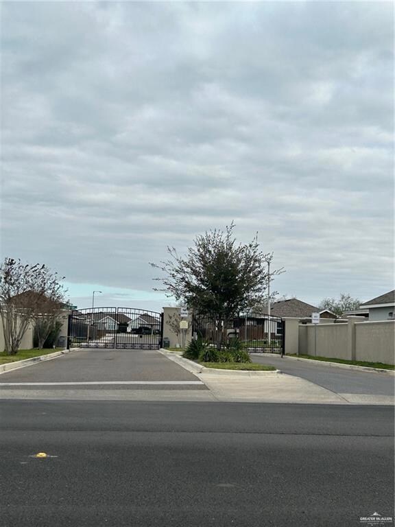 View of asphalt street featuring a gate, a gated entry, curbs, and street lighting