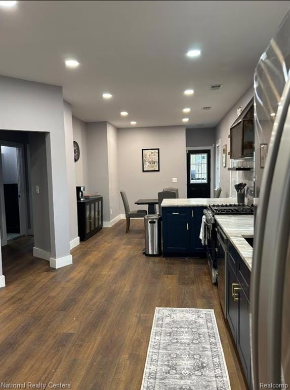 Kitchen with a peninsula, recessed lighting, appliances with stainless steel finishes, dark wood-type flooring, and light stone counters