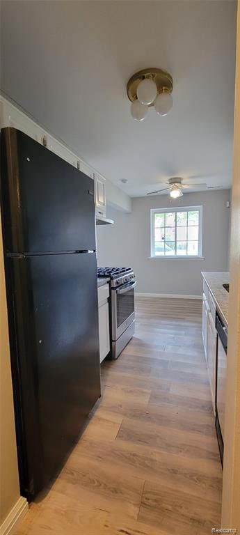 Kitchen with white cabinets, freestanding refrigerator, stainless steel gas range, light wood finished floors, and under cabinet range hood