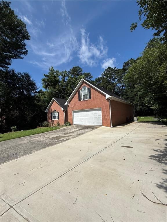 View of home's exterior featuring brick siding, driveway, and view of scattered trees