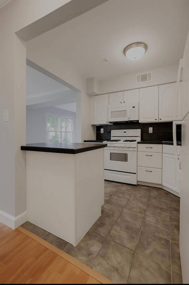Kitchen featuring white appliances, dark countertops, white cabinets, backsplash, and a peninsula