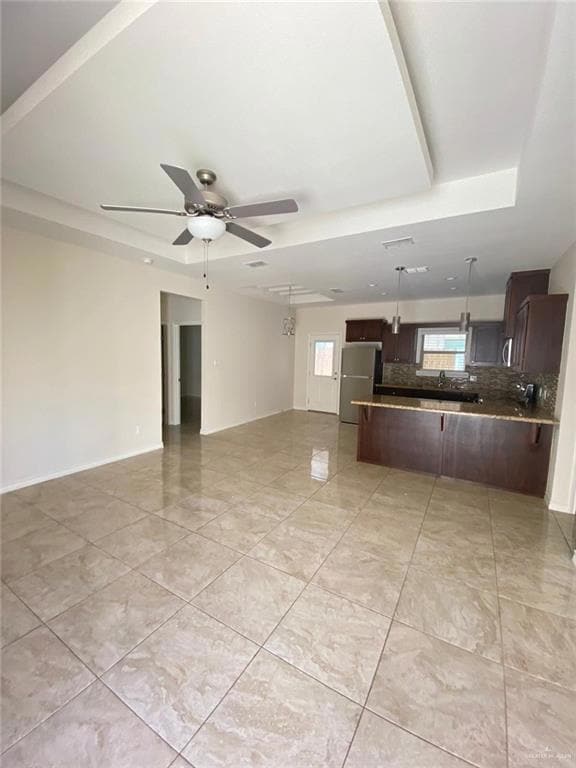 Unfurnished living room featuring a ceiling fan, a raised ceiling, and light tile patterned flooring