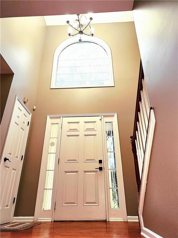 Foyer entrance featuring healthy amount of natural light, a towering ceiling, wood finished floors, and a chandelier