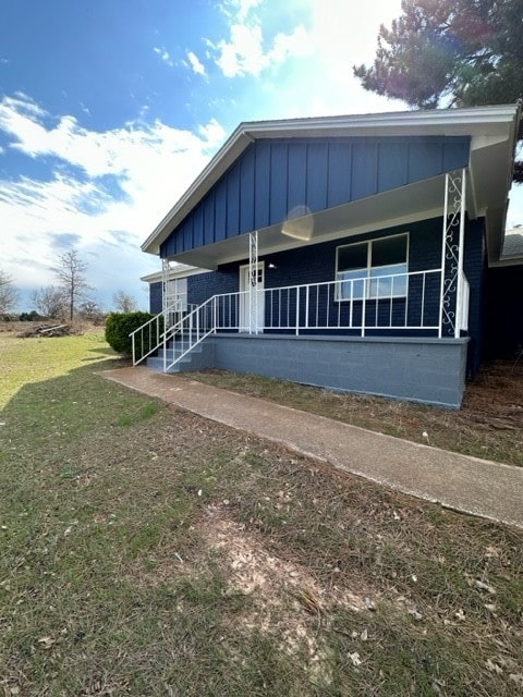 View of front facade featuring board and batten siding, covered porch, and a front yard