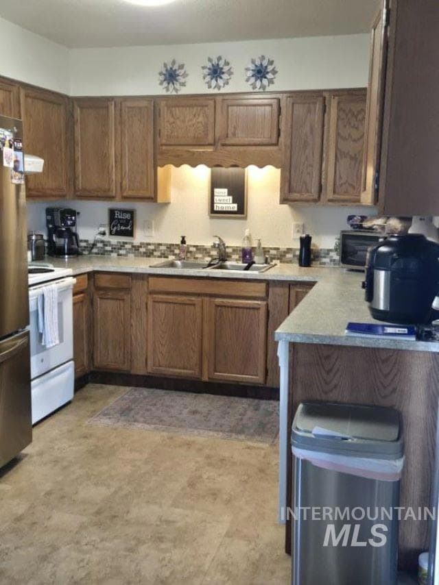 Kitchen featuring white electric range oven, freestanding refrigerator, light countertops, and brown cabinets