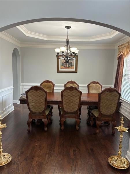 Dining area with arched walkways, a tray ceiling, ornamental molding, dark wood finished floors, and wainscoting
