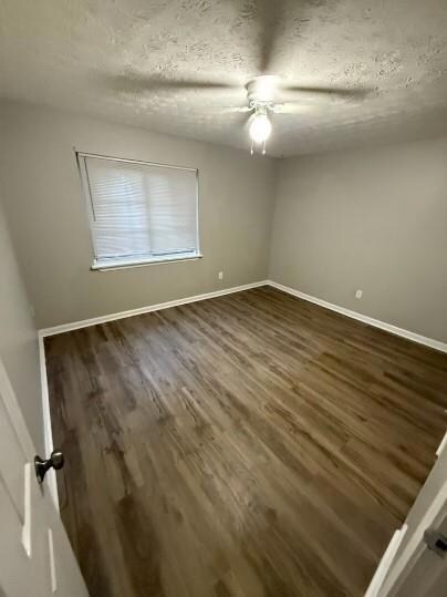 Unfurnished room featuring ceiling fan, baseboards, and dark wood-style floors